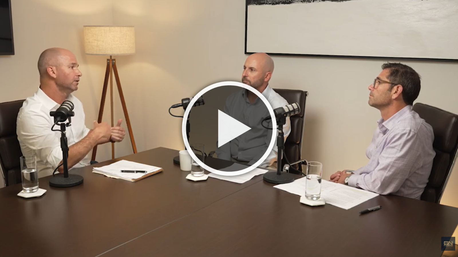 Three men talking in a room with play button overlay