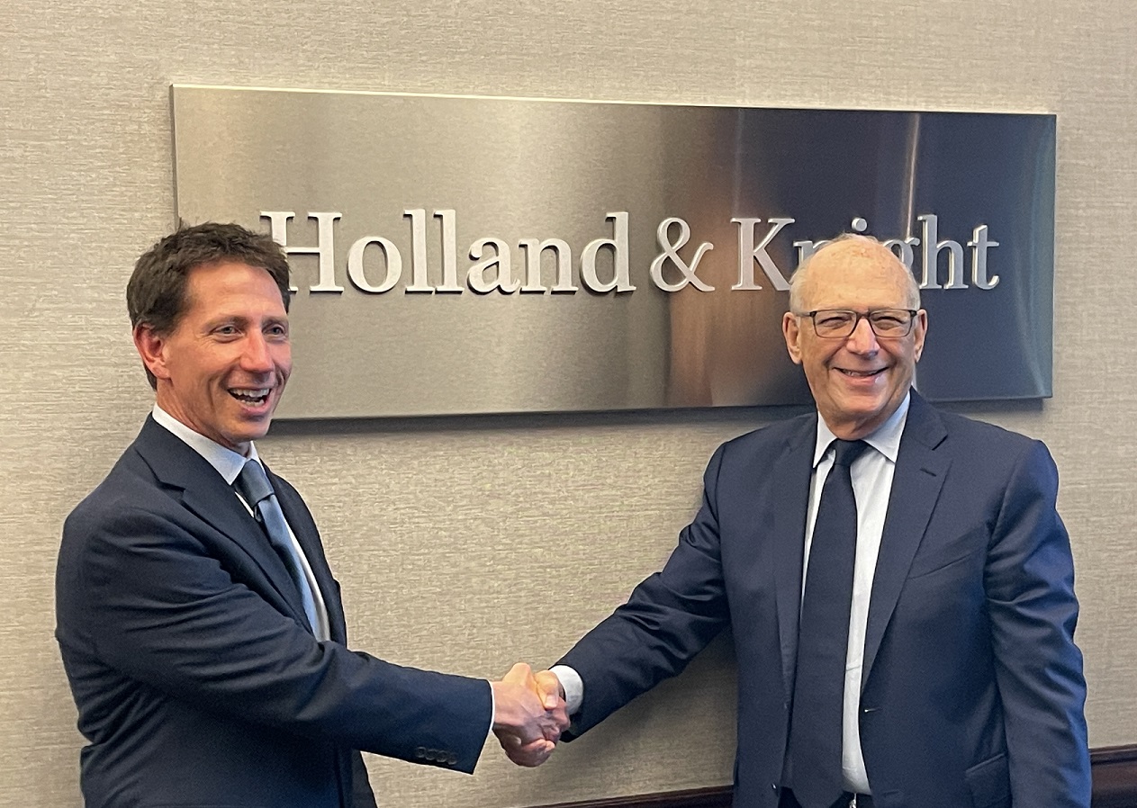Matt Burnstein and Steve Sonberg shaking hands in front of Holland & Knight logo