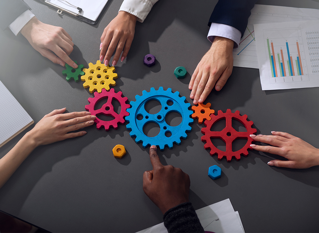 6 hands reaching towards different colored gears on table