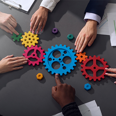 6 hands reaching towards different colored gears on table