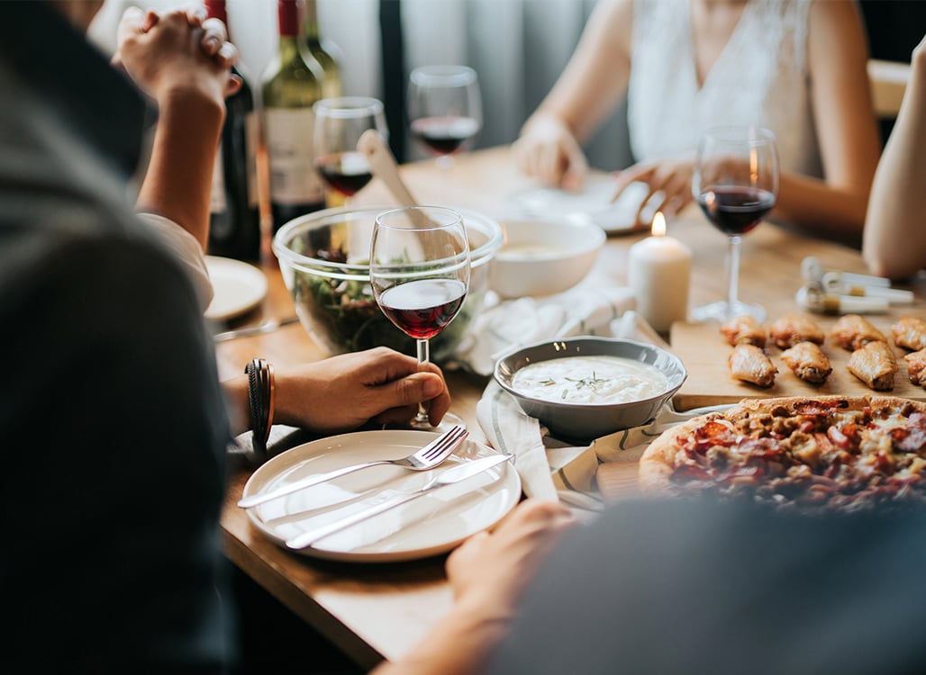 Hand holding wine glass, green salad in glass bowl, pizza on plate