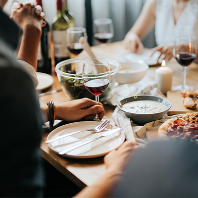 Hand holding wine glass, green salad in glass bowl, pizza on plate